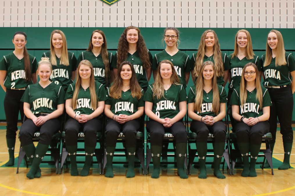 Softball team posing in a gym half of them are in chairs and the other half are standing behind them