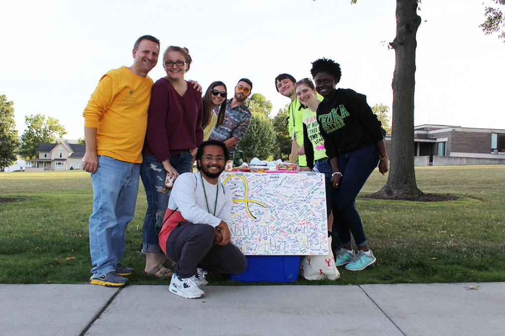 Rev. Eric Detar, College chaplain (left) and group of students gather in front of a poster, signed by dozens of students showing support for those affected by suicide at the 2017 One Walk. Samy Hamdan '19 (kneeling in front) has helped organize the event for three years.