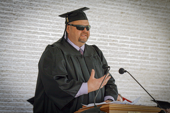 Guy in his cap and gown speaking at a podium at graduation